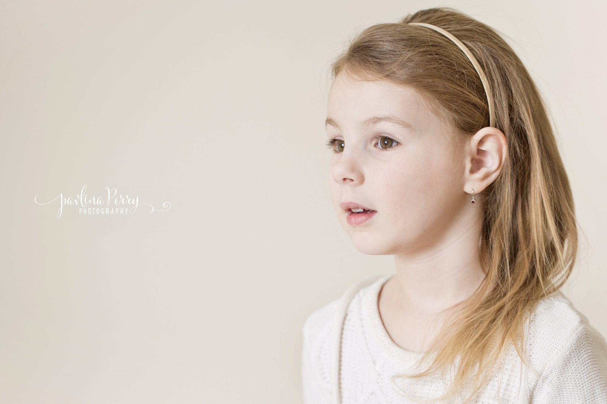 Girl in a white top looking sideways against a soft neutral studio background