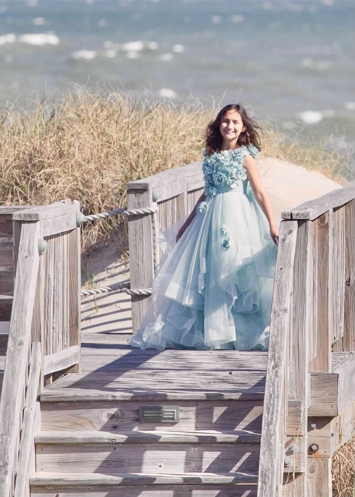 Girl in a pale blue gown standing on a wooden boardwalk through the dunes