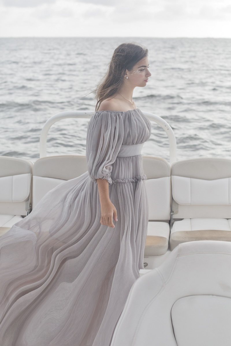 Portrait in a flowing gray gown aboard a boat, with the sea in the background