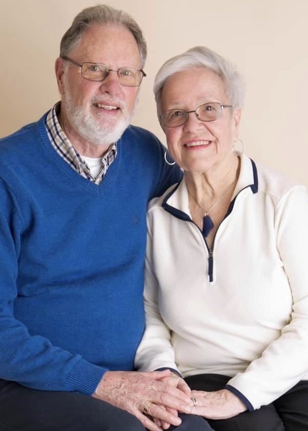 Smiling older couple sitting close together and holding hands, wearing blue and ivory