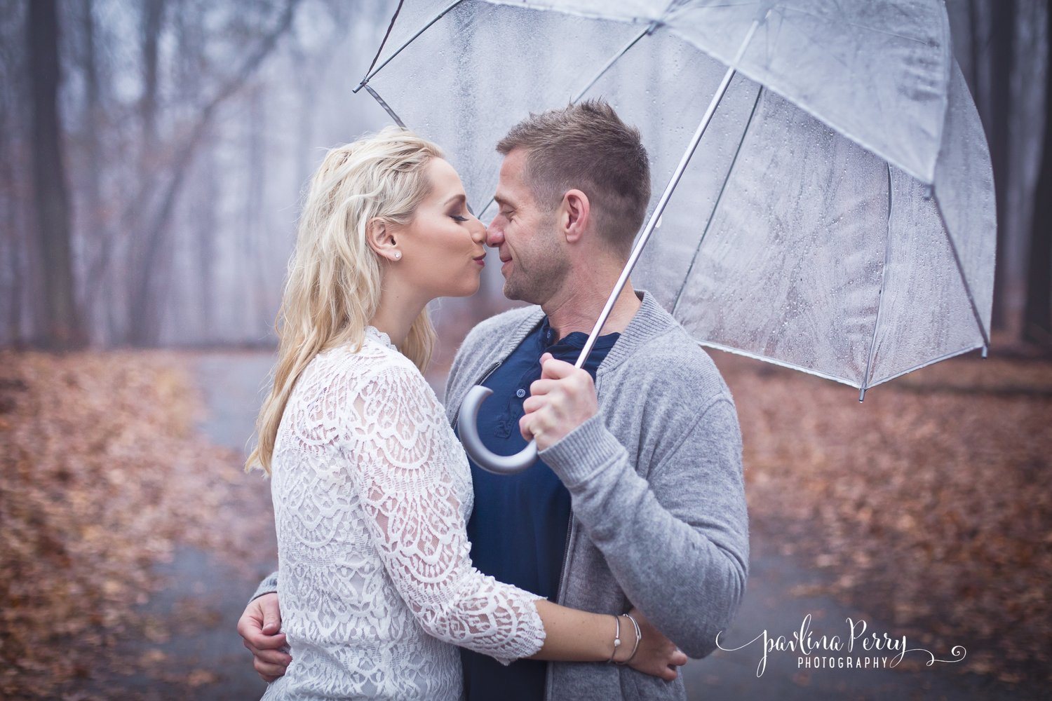 Couple sharing a tender moment under a transparent umbrella in woodland