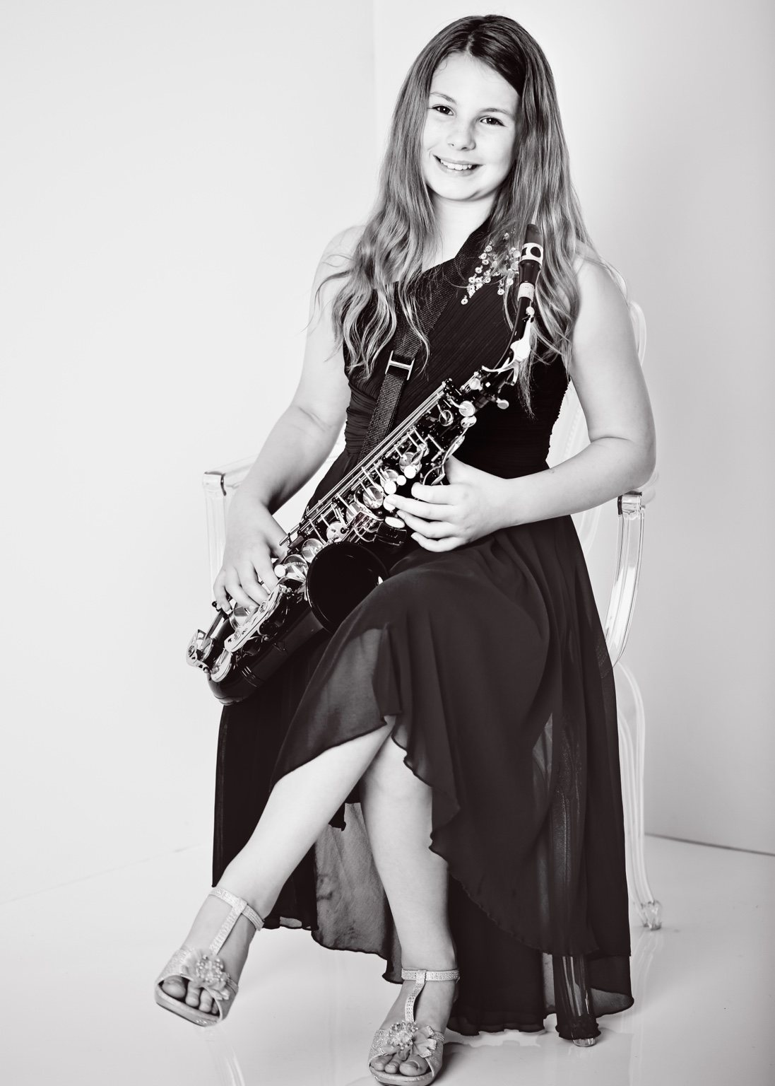 Black-and-white studio portrait of a smiling girl in a dark dress holding her saxophone