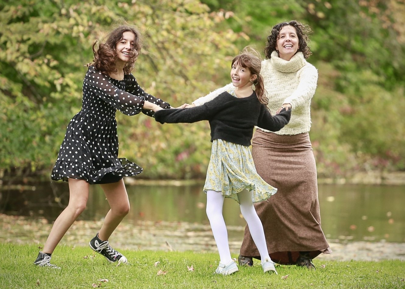 Three family members holding hands and laughing beside a lake