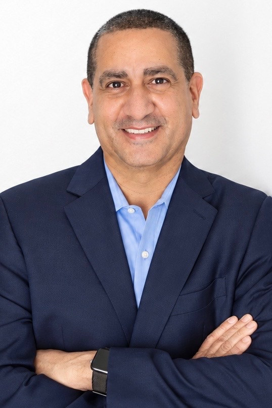 Smiling man in a navy suit with arms crossed against a white background