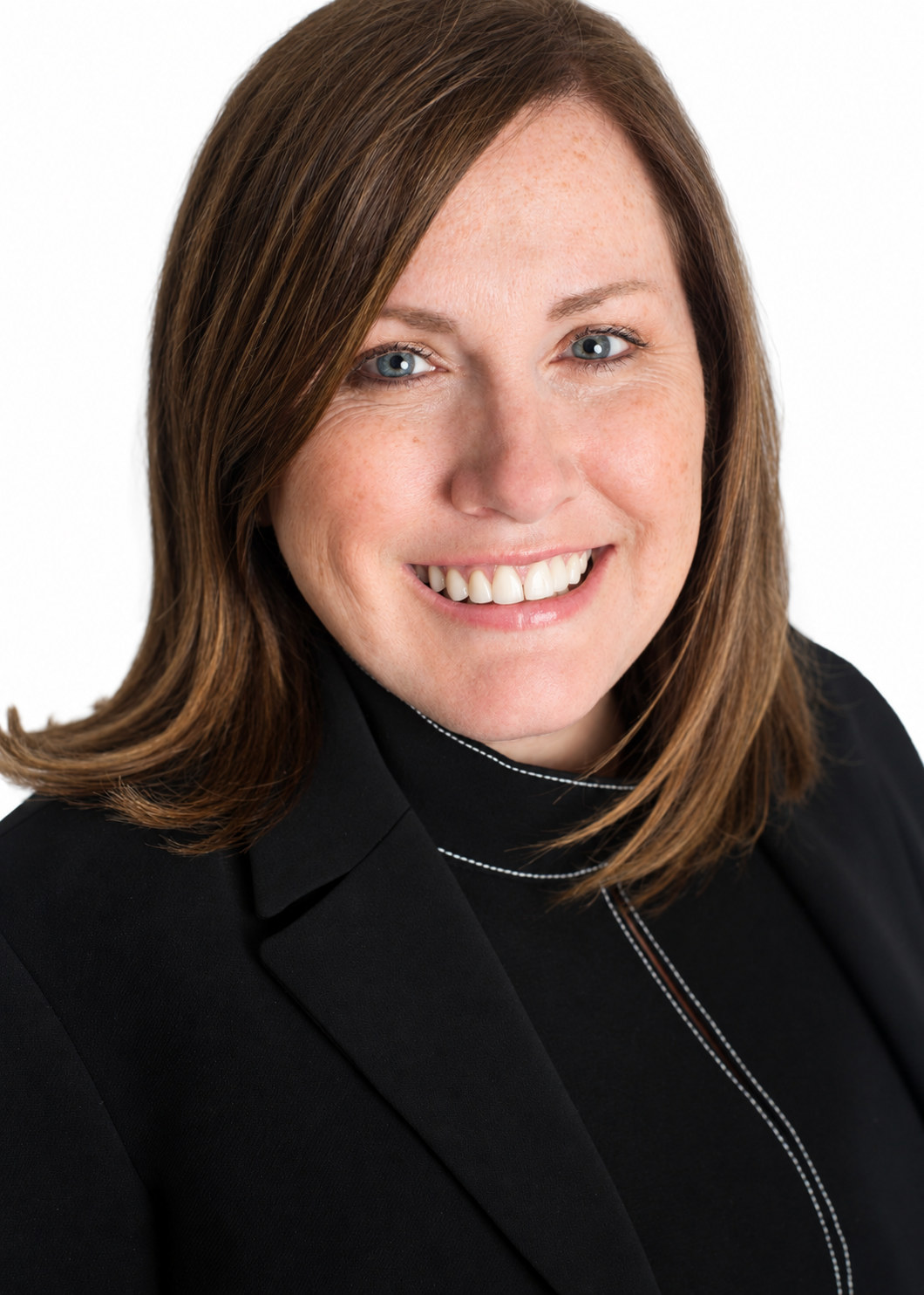 Smiling woman with shoulder-length brown hair in a black jacket against a white background