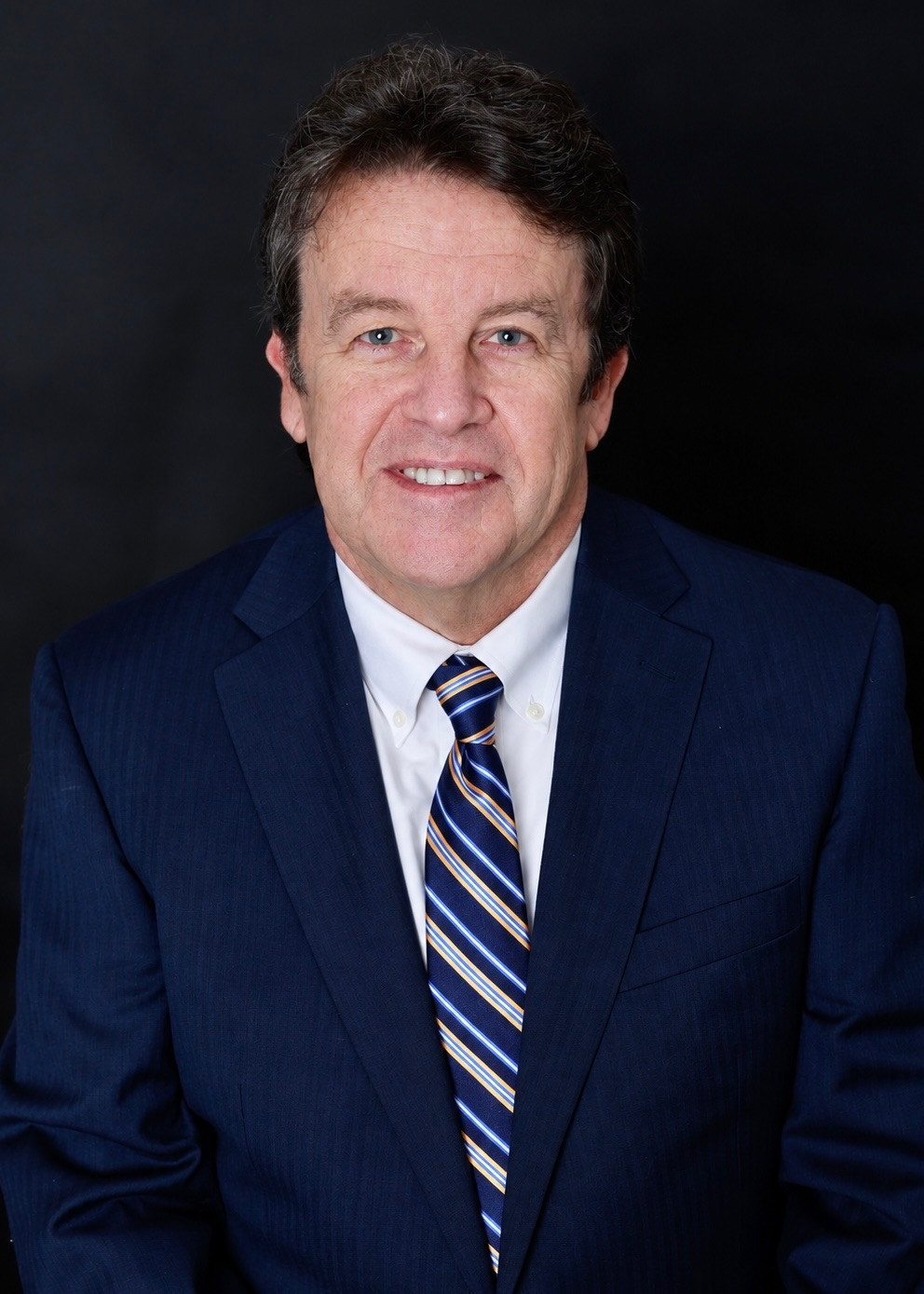 Smiling man in a navy suit and striped tie against a black background
