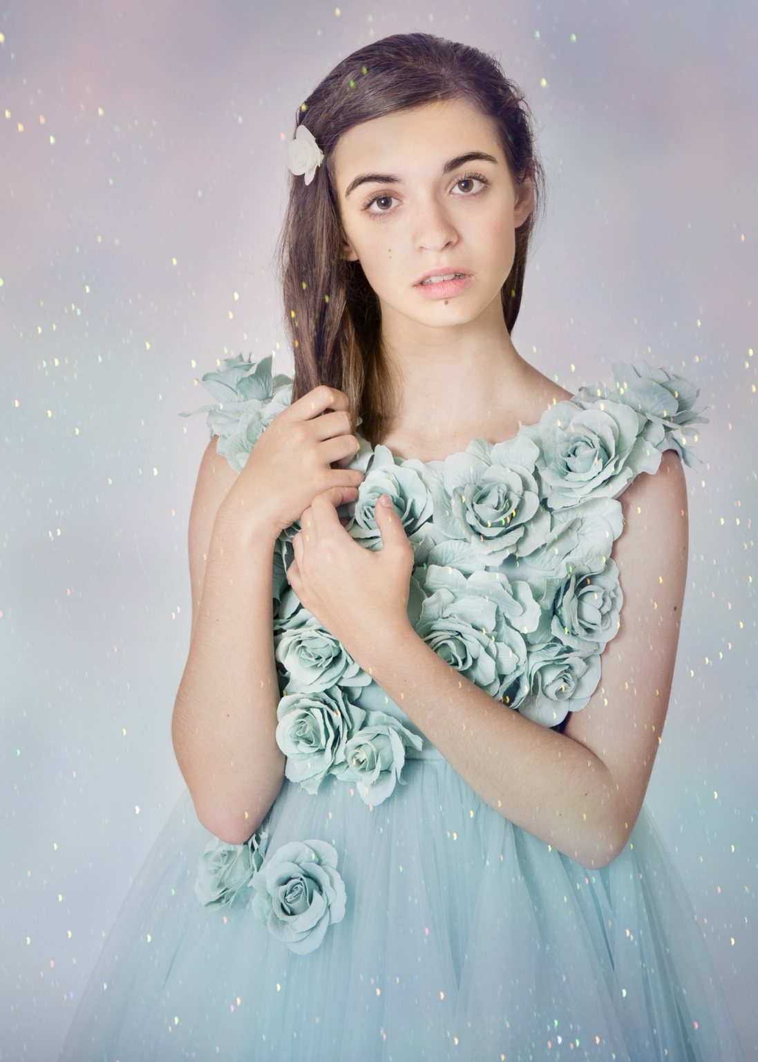 Studio portrait of a girl in a pale green dress with floral details and glitter around her