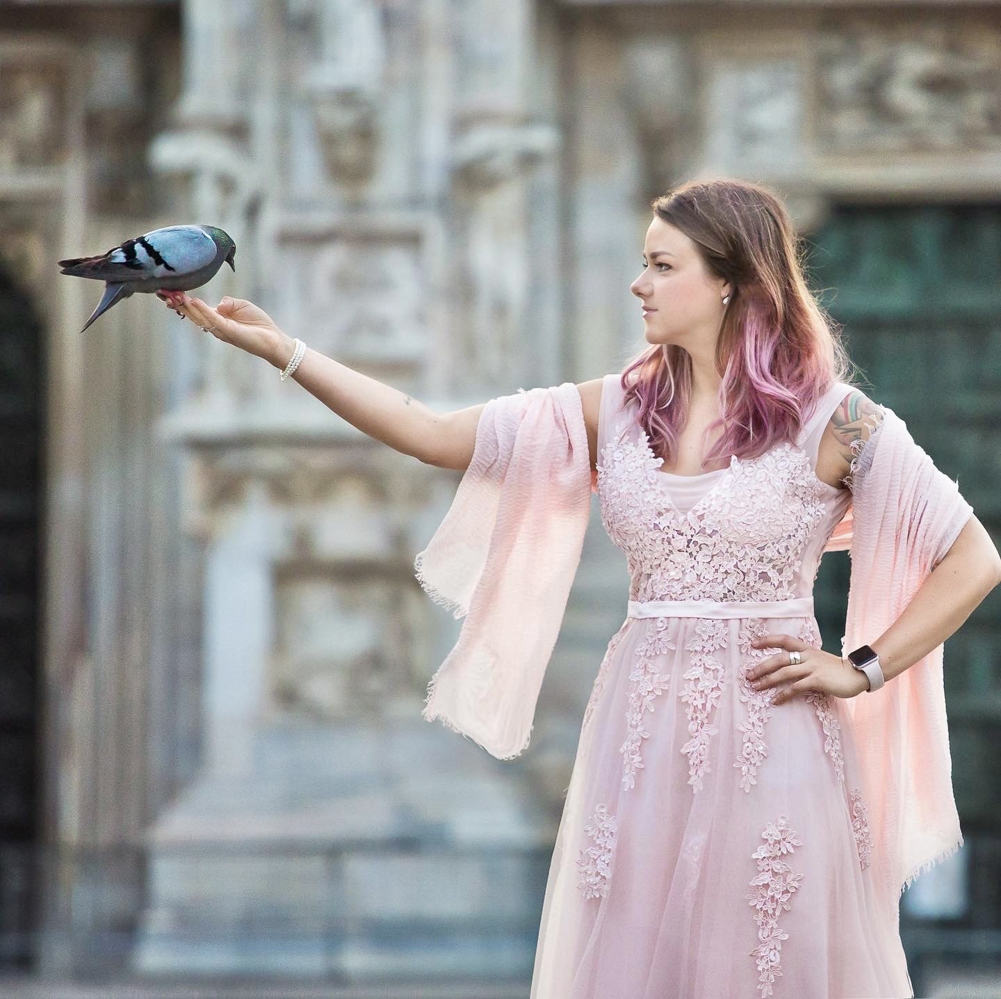 Woman in a pale pink lace gown holding a pigeon on her outstretched hand