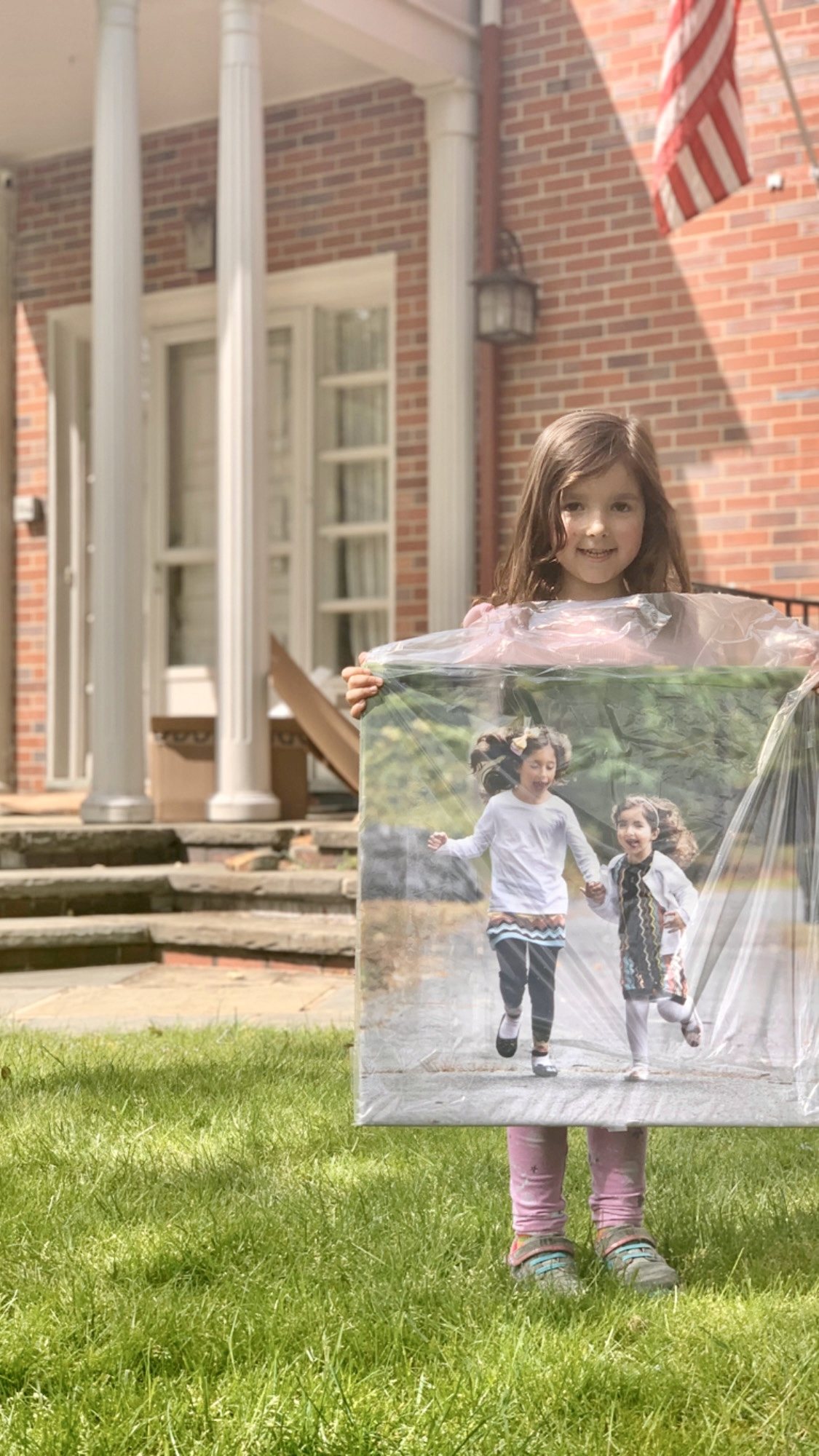 Child holding a large wrapped portrait print of two children running together