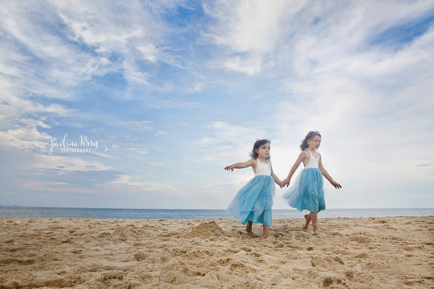 Two girls holding hands in blue dresses on the beach