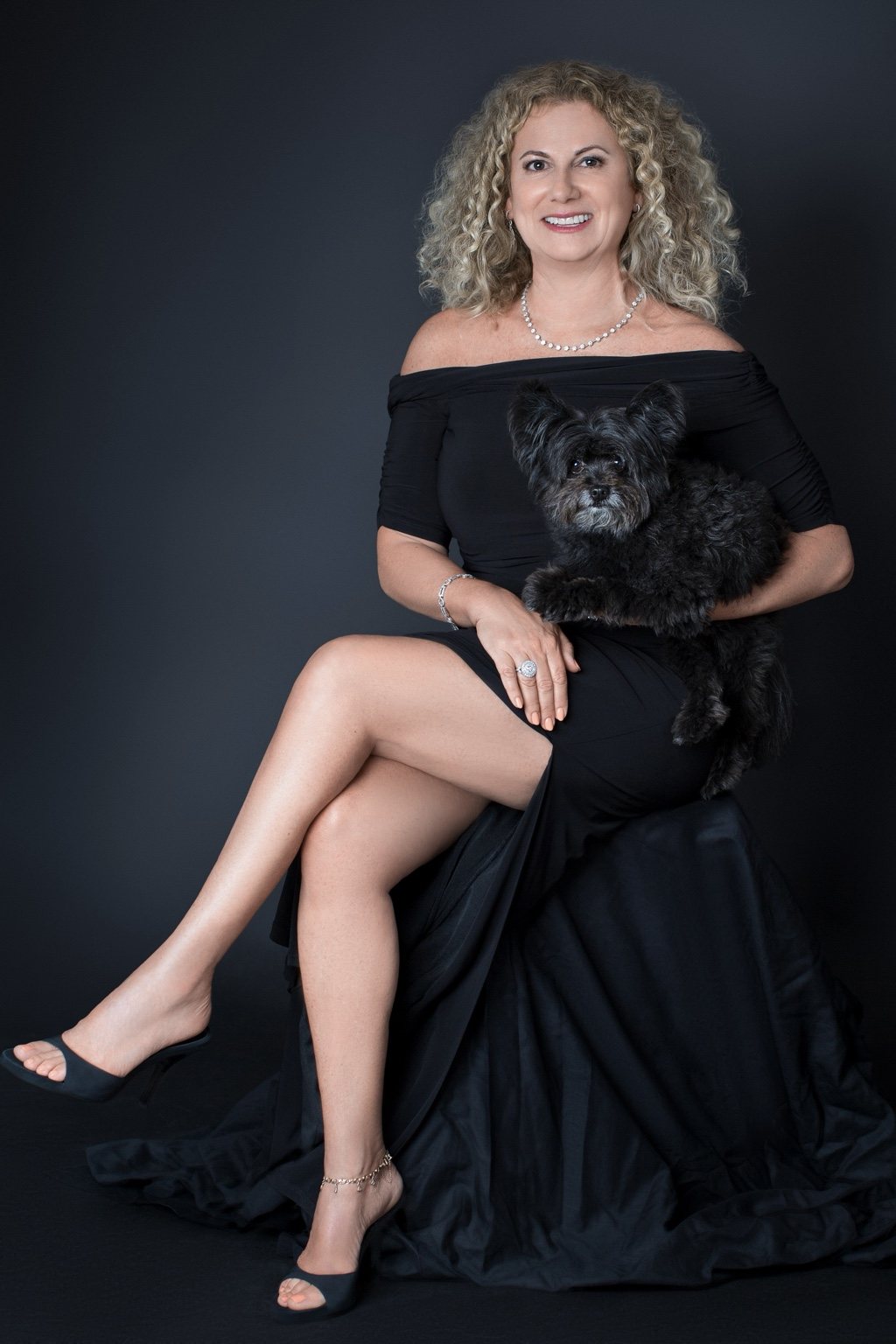 Full-length seated portrait of a woman in a flowing black dress with her small dog