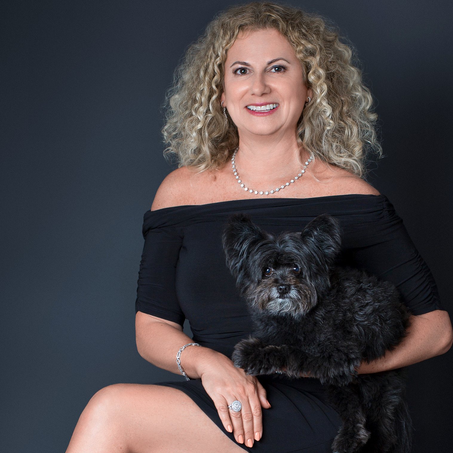 Woman in a black dress holding her small black dog in the studio