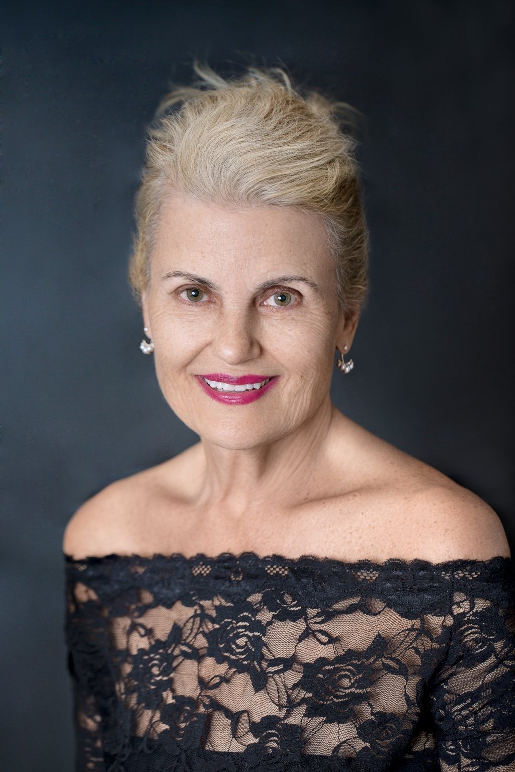 Close studio portrait of a smiling woman in black lace against a dark background